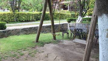 Un conjunto de columpios de madera en un jardín con un muro de piedra y bancos de metal.