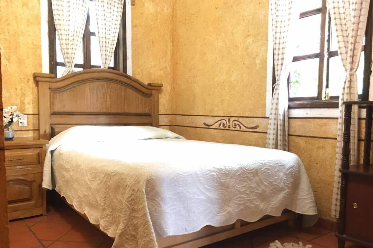 A bedroom with a wooden bed, a nightstand, a dresser, and a window with curtains.