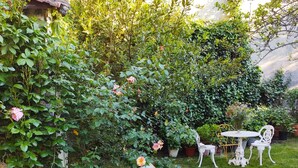 Een tuin met twee ligstoelen en een bijzettafeltje, omringd door weelderig groen en bloeiende planten.