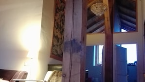 Een rustieke kamer met een houten plafond, een bed met een blauwe deken, een stoel en een tafel.