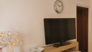 Ein Zimmer mit einem Holztv-Schrank, einem Flachbildfernseher, einer Wanduhr und einer dekorativen Holzreliquie.