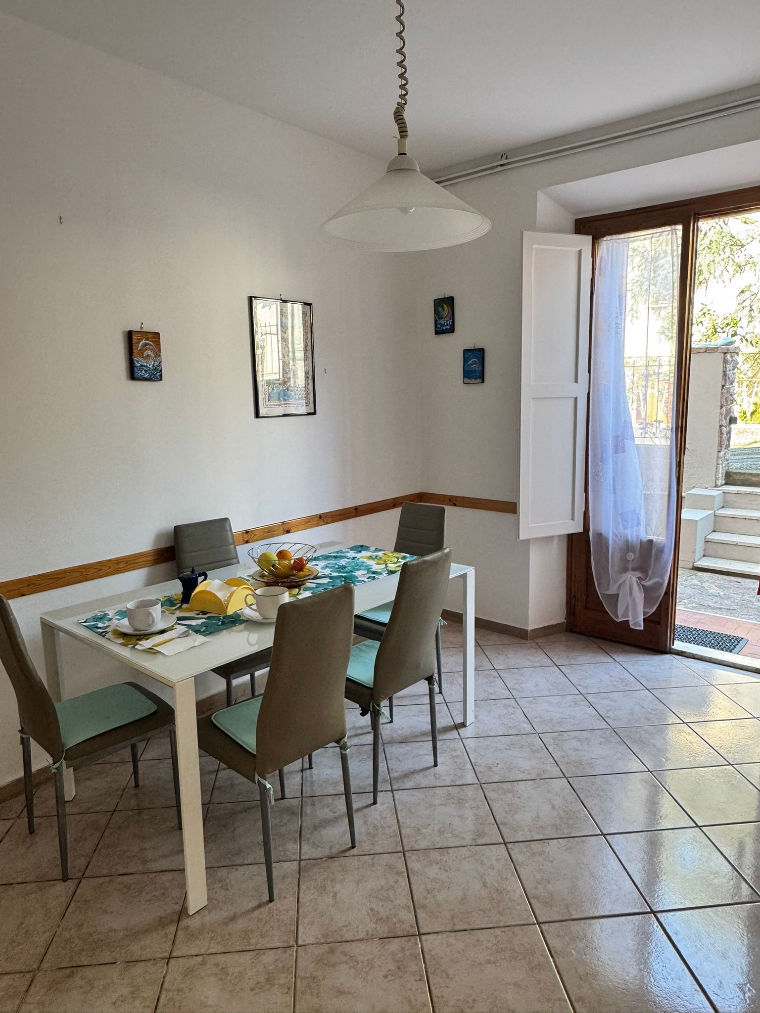 Comedor con mesa dispuesta para cuatro, sillas, lámpara colgante y puerta que da al exterior.