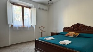 Ein Schlafzimmer mit einem hölzernen Bett, einem Fenster mit Vorhängen, einer Klimaanlage und einer Pendelleuchte.
