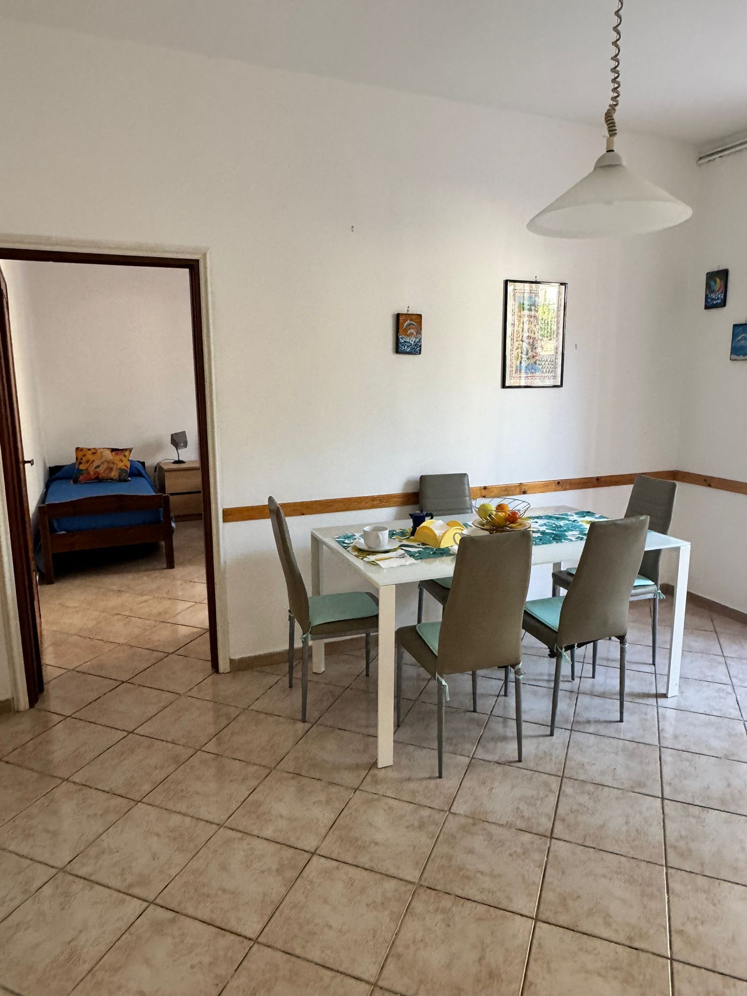 Un comedor con mesa y sillas, una lámpara colgante y una cama al fondo.