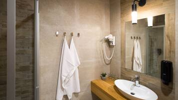 A modern bathroom with a glass shower, a wooden vanity, a white sink, and a mirror with a light fixture.