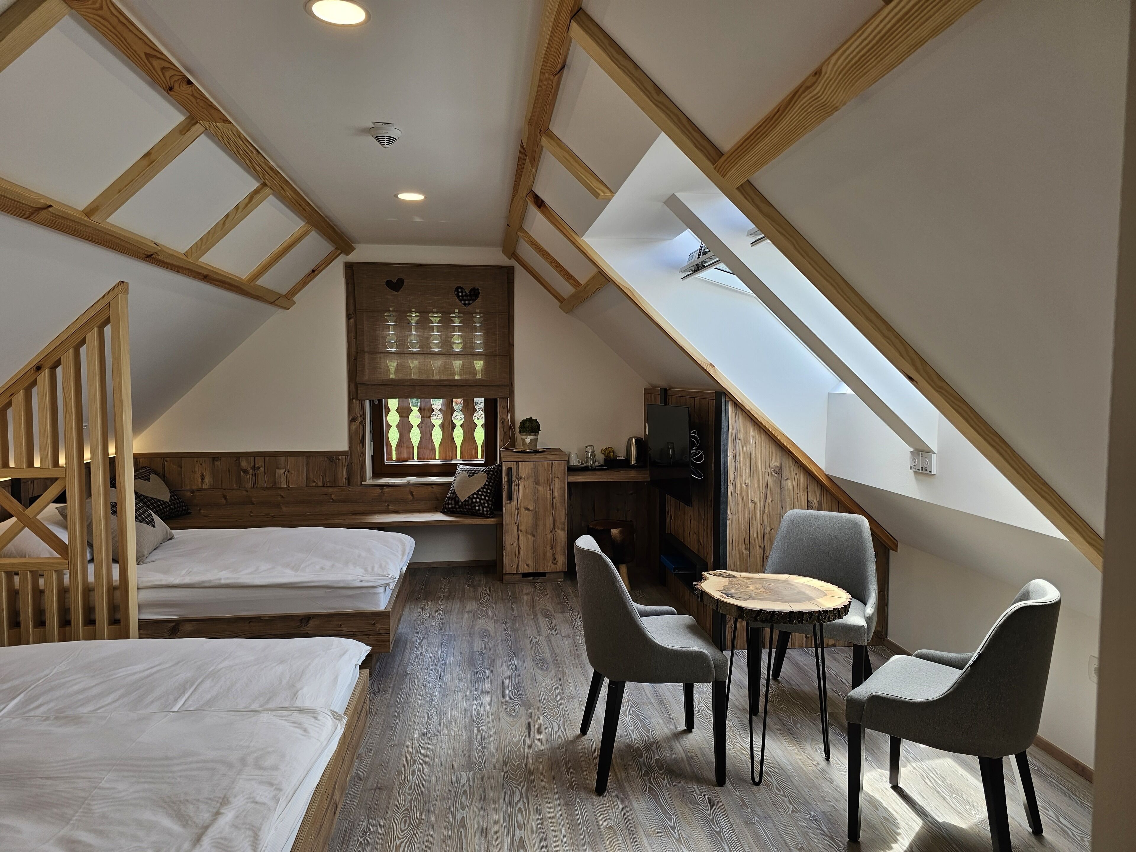 Ein gemütliches Schlafzimmer im Dachgeschoss mit Holzbalken, einem Schlafsofa, einem kleinen Esstisch und zwei Stühlen.