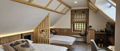 A cozy attic bedroom with two beds, wooden beams, a skylight, and a small dining area.