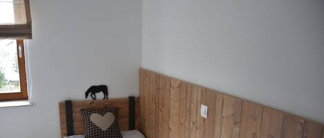 A single bed with a wooden headboard, a heart-shaped pillow, and a small black silhouette decoration on the headboard.