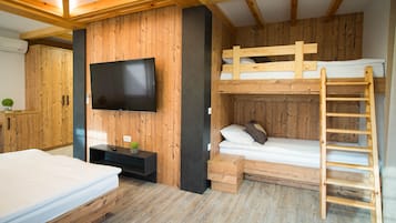 A room with a bunk bed, a TV mounted on the wall, wooden flooring, and a ladder for the upper bunk.