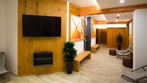 A modern interior with a wooden wall, a flat-screen TV, a bench, and a lounge area with chairs and a potted plant. - Penzion Pr Anzl (Bled)