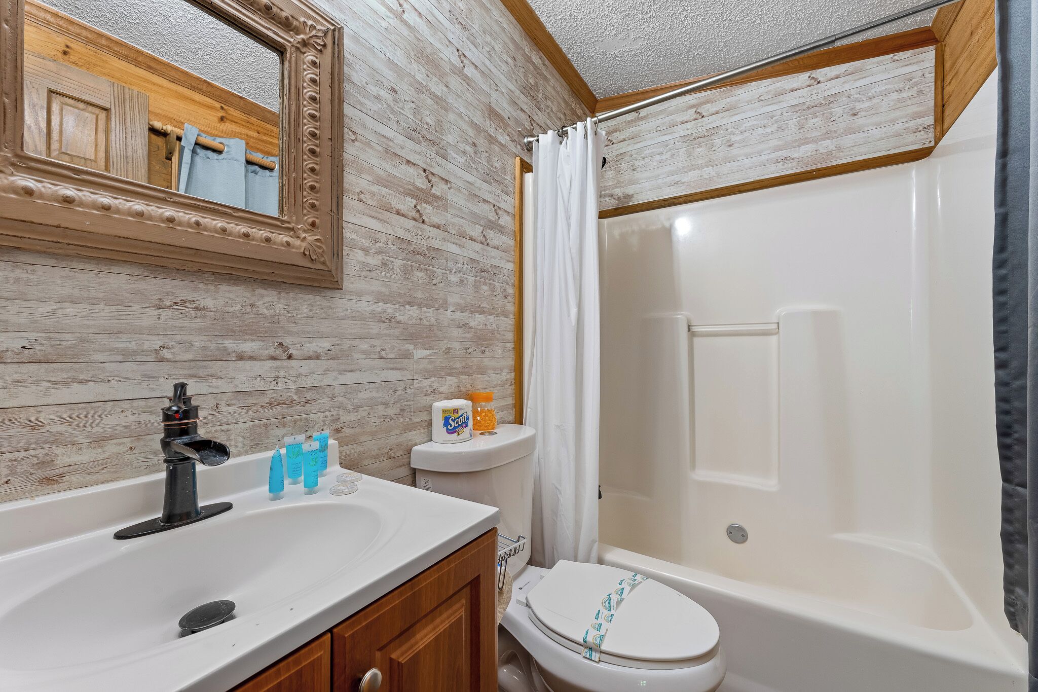 A bathroom with a wooden wall, a white sink, a toilet, and a bathtub.