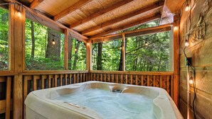 Una terraza de madera con un jacuzzi, rodeada por una barandilla de madera, con vista a un bosque.