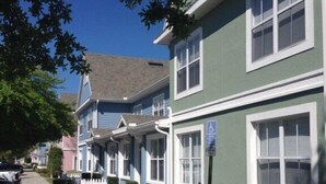 Une rangée de maisons à deux étages, avec un revêtement extérieur vert et des bordures blanches, un trottoir et une clôture blanche en piquets.