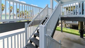 A covered outdoor area with a white railing, a staircase, and a concrete floor.