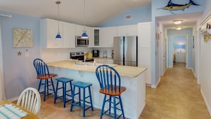 A modern kitchen with white cabinets, a central island with bar stools, a microwave, and a refrigerator.
