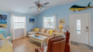 A living room with a beige sofa, a brown leather chair, a ceiling fan, and a fish mural on the wall.