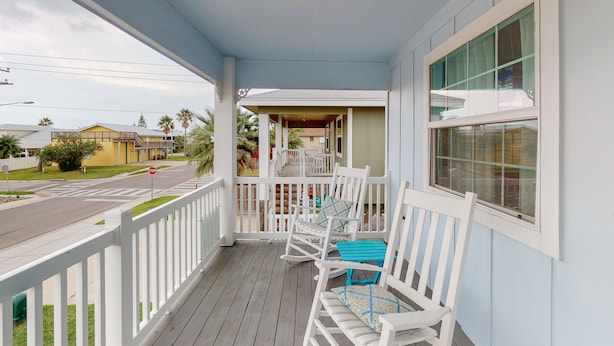 A porch with white railings and two rocking chairs, one with a blue cushion.