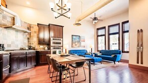 Una cocina moderna con armarios oscuros, una mesa de comedor y un sofá azul en un amplio salón con ventanas grandes.