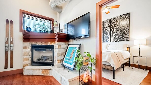 Una habitación acogedora con chimenea de piedra, un televisor montado encima y una cama con mesita de noche, además de una gran obra de arte en la pared.