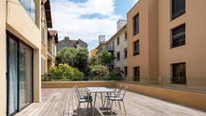 Een houten terras met een tafel en stoelen, omringd door gebouwen met balkons en groen.