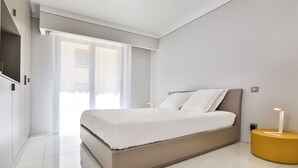 Een moderne slaapkamer met een groot bed, een nachtkastje met een kaars, en uitzicht naar buiten door een raam.