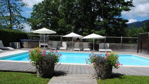 Ein Swimmingpool mit Liegestühlen und Sonnenschirmen, umgeben von einer Holzterrasse und Kübelpflanzen.