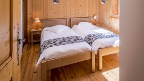 Ein Zimmer mit Holzwänden und -böden, zwei Betten, einem Nachttisch mit Lampe und einem Fenster.