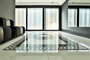 Eine moderne Lobby mit spiegelndem Boden, großen Fenstern und einer Sitzecke mit grau und schwarz gepolsterten Stühlen.
