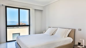 A modern bedroom with a large bed, a nightstand, and a view of a cityscape through a large window. - T2 sea view "Mare e Sole (Ajaccio)