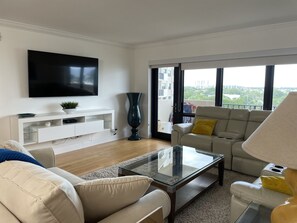 A modern living room with a flat-screen TV, a glass coffee table, and a sofa.