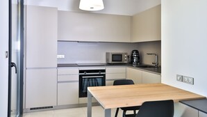 Een kleine keuken met een magnetron, koffiezetapparaat en een spoelbak. Er staat een tafel met stoelen en een raam met uitzicht.