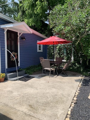 Une terrasse avec une table et des chaises, un parasol rouge et une maison avec une boîte aux lettres et le numéro 324.