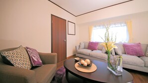 A living room with a brown sofa, a grey sofa, and a round coffee table with a vase and decorative items. - Roof Villa Shin-Imamiya (Osaka)