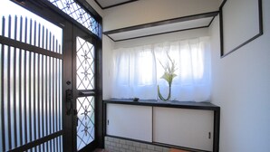 A room with a sliding door, a window with sheer curtains, a small table, and a vase with a plant. - Roof Villa Shin-Imamiya (Osaka)