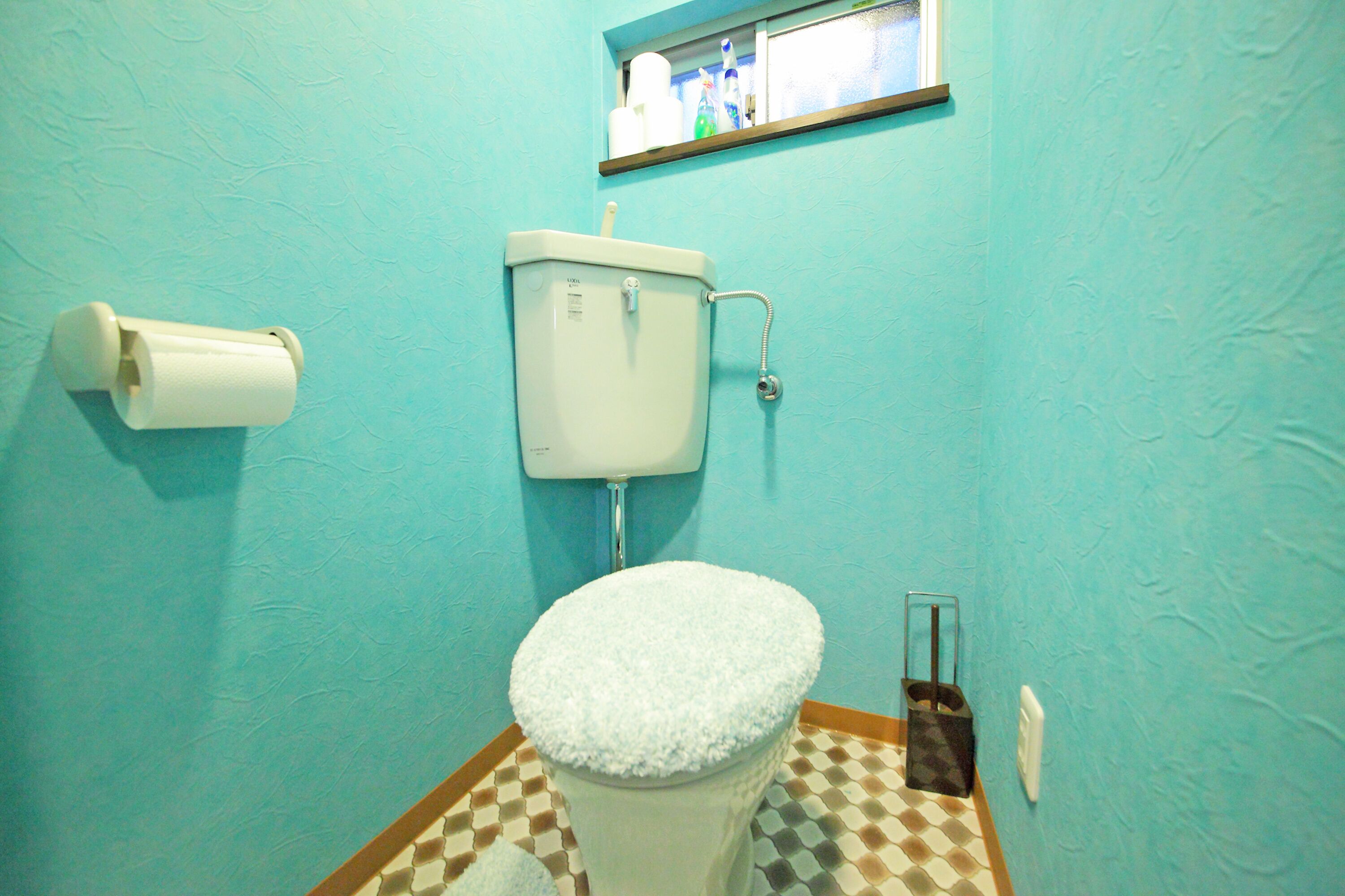 A bathroom with a toilet, a roll of toilet paper, and a small shelf above the toilet.