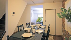 A dining area with a table set for six, chairs, a plant, and a staircase leading to another room. - Roof Villa Shin-Imamiya (Osaka)