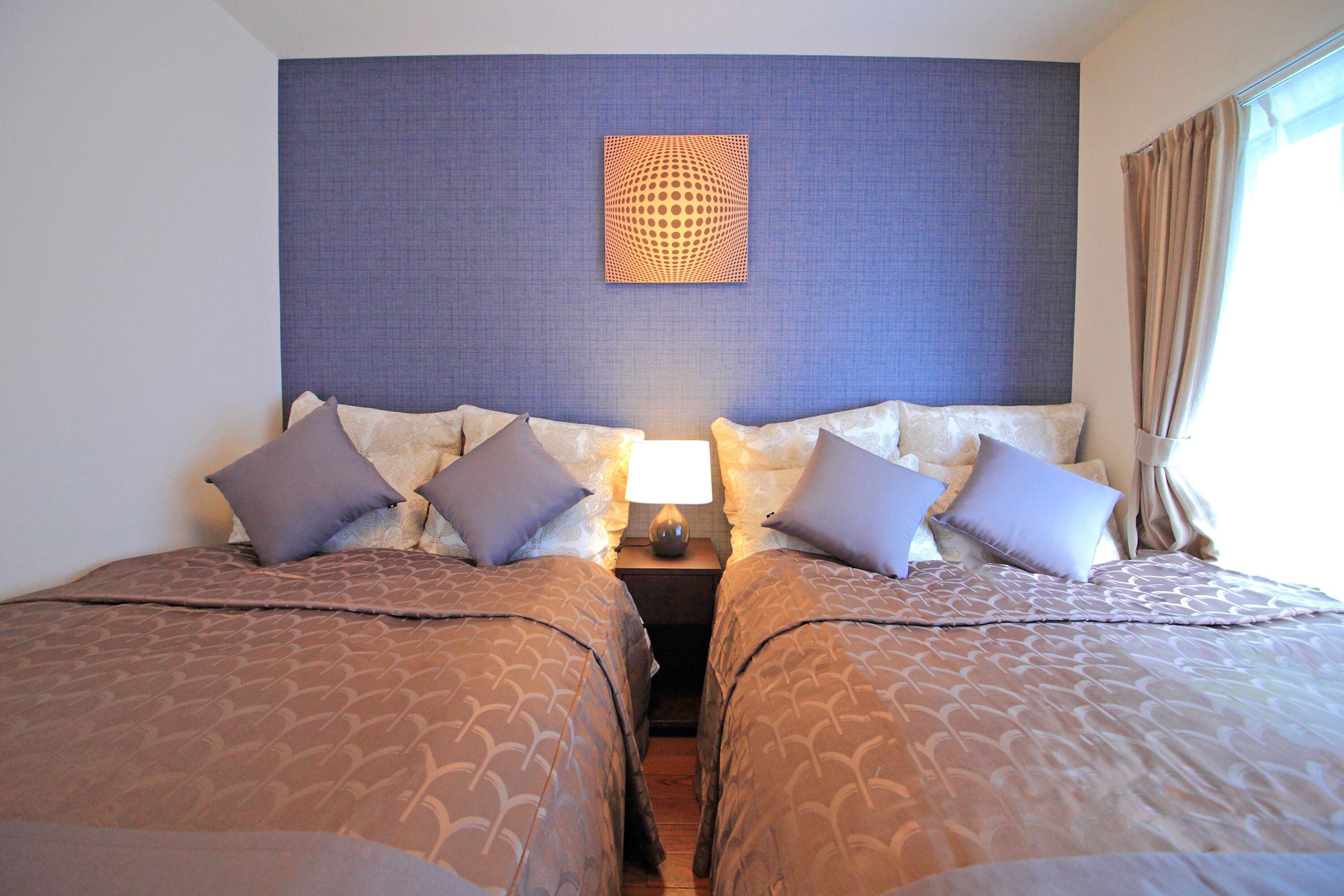 Ein Hotelzimmer mit zwei Betten, einem Kopfteil mit geometrischem Muster und einem Nachttisch mit Lampe.