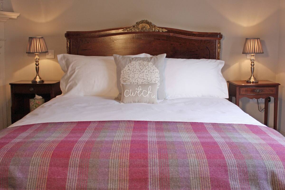 A neatly made bed with a plaid bedspread, two bedside lamps, and a decorative pillow with the word "cutch" on it.
