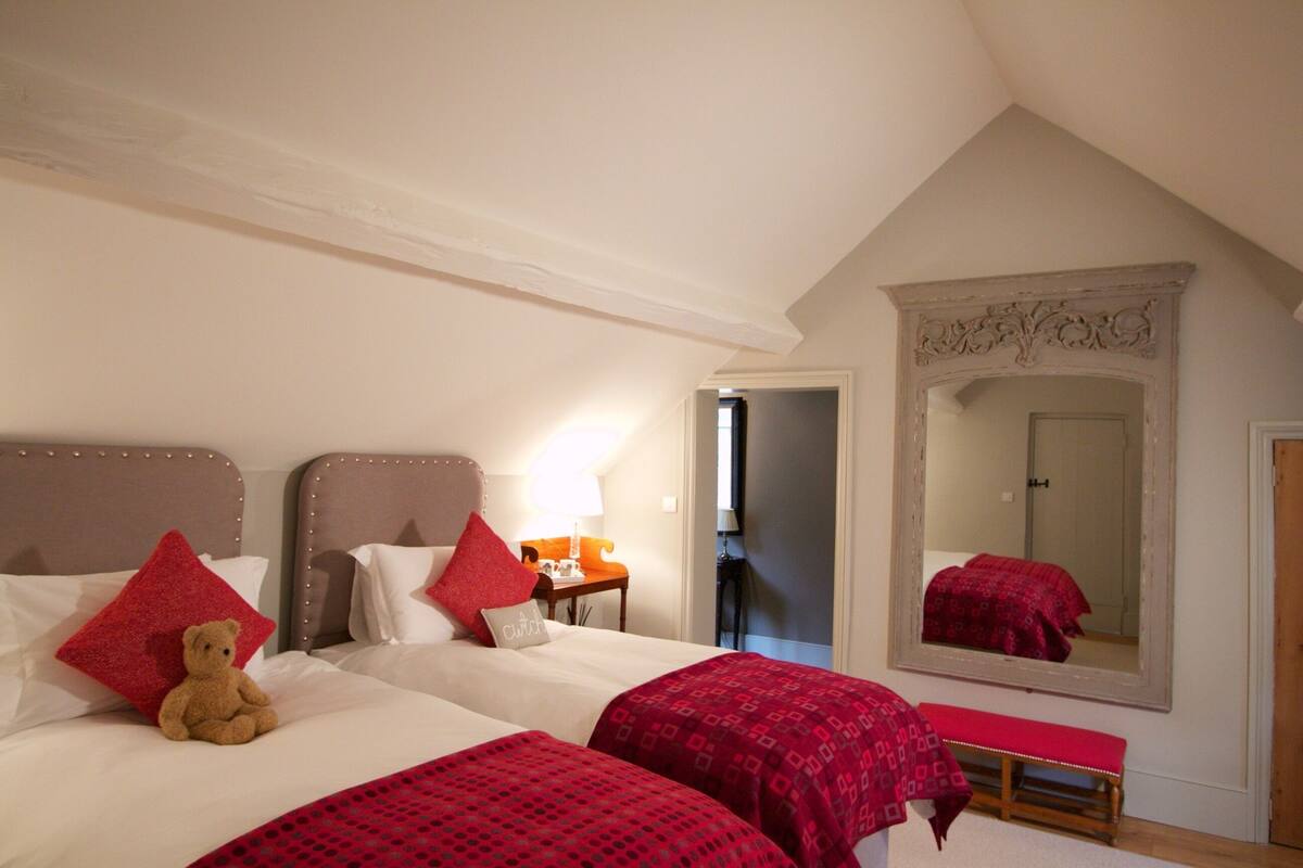 A bedroom with two beds, a large mirror, and a teddy bear on one bed.