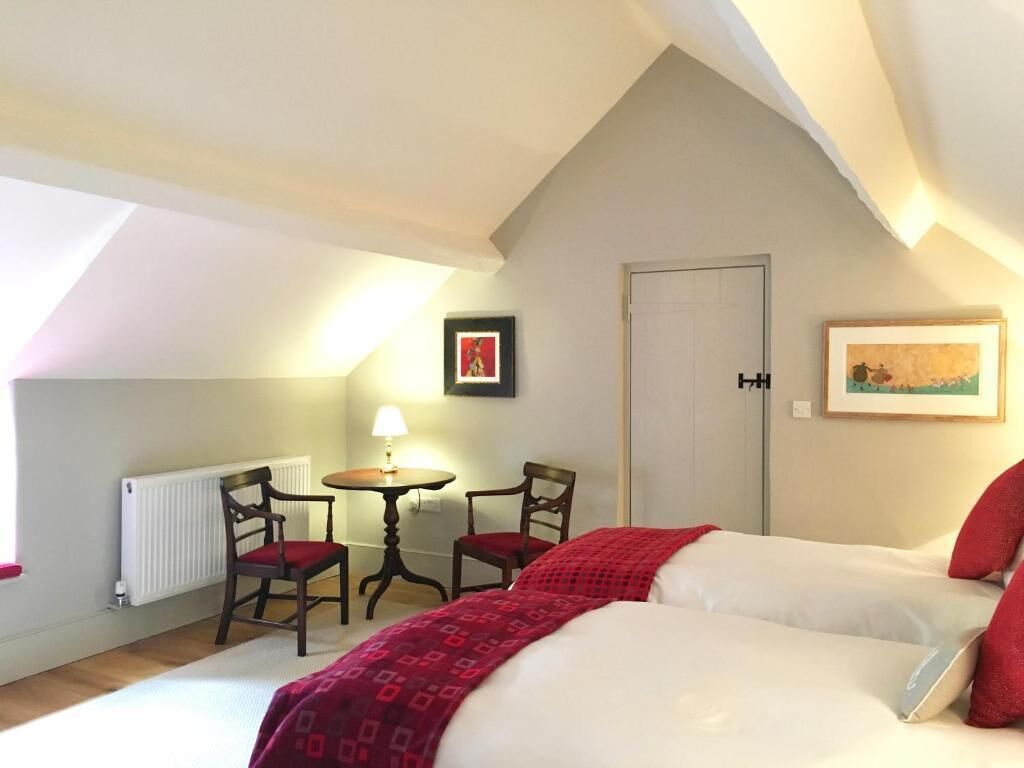A bedroom with a bed, two chairs, a small table with a lamp, a radiator, and a door.