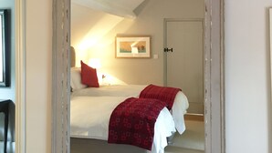 A bedroom with a large mirror, a bed with white linens, a red throw blanket, and a framed picture on the wall. - The Old Stores (Montgomery)