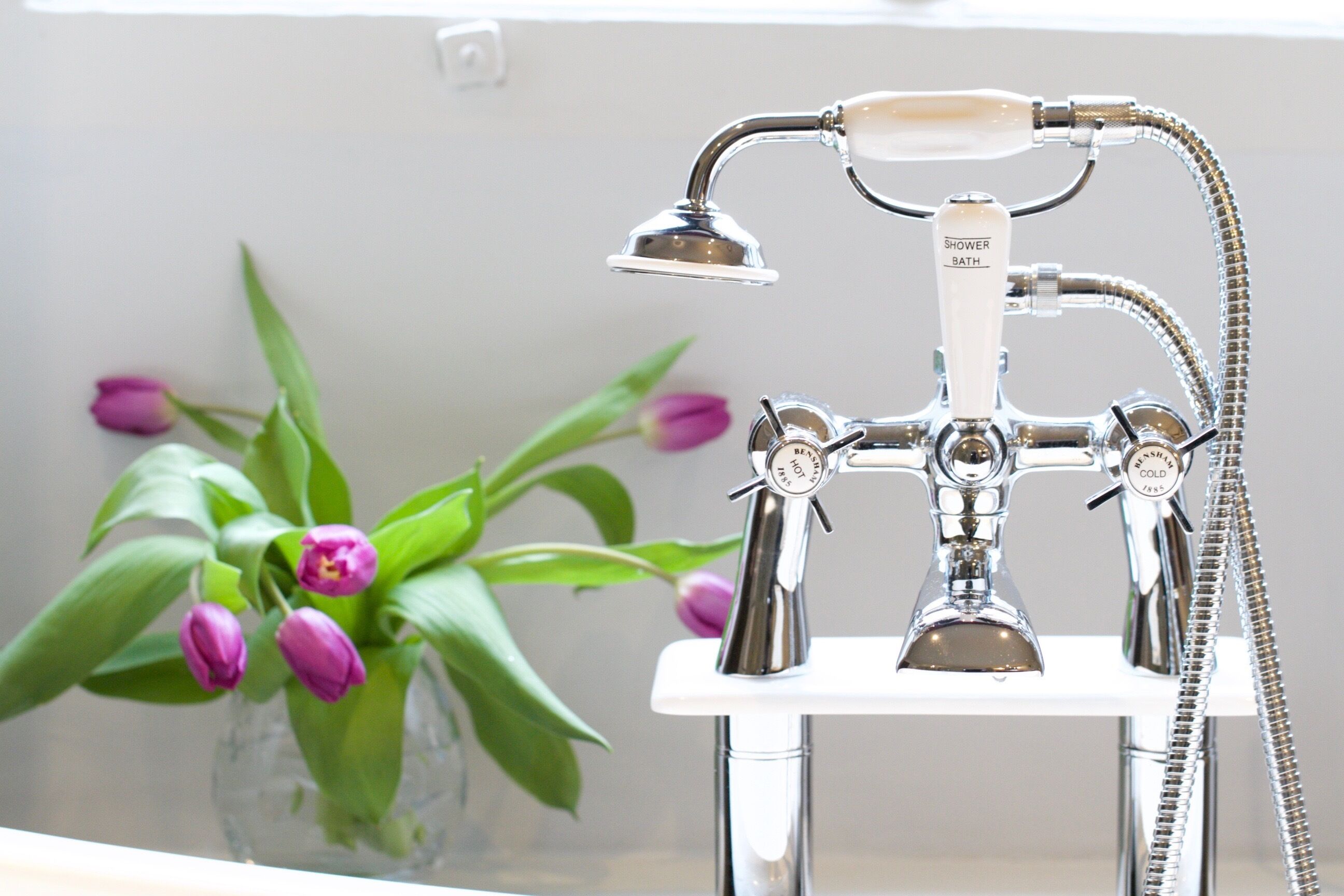 A bathroom with a vintage-style shower and a glass vase with purple flowers on the counter.