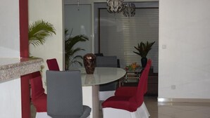 Uma sala de jantar com uma mesa redonda, cadeiras vermelhas e brancas e um vaso.