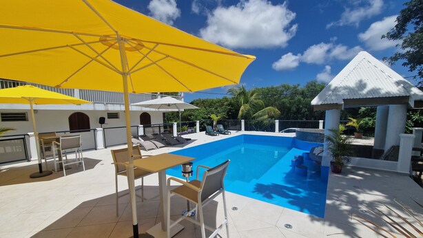 Uma área de piscina com guarda-sol amarelo, espreguiçadeiras e uma pequena mesa.