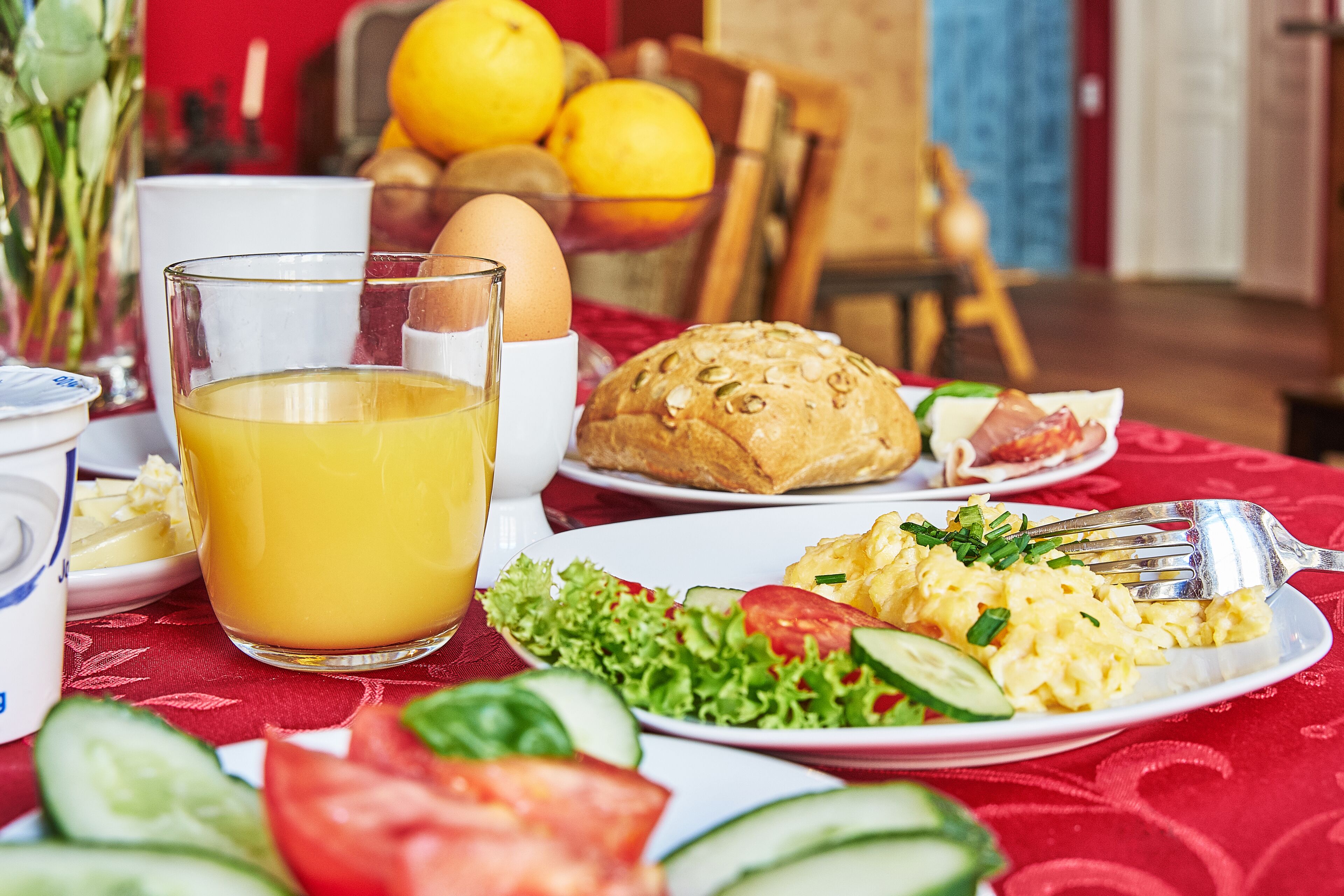 Ein Frühstückstisch mit Orangensaft, Eiern, Brot und einem Teller mit Eiern und Gemüse.