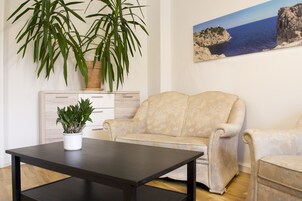 A living room with a beige sofa, a black coffee table, and two potted plants.
