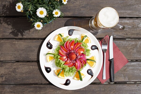 A plate of food with a salad and fruit, a knife, fork, and a glass of beer on a wooden table.