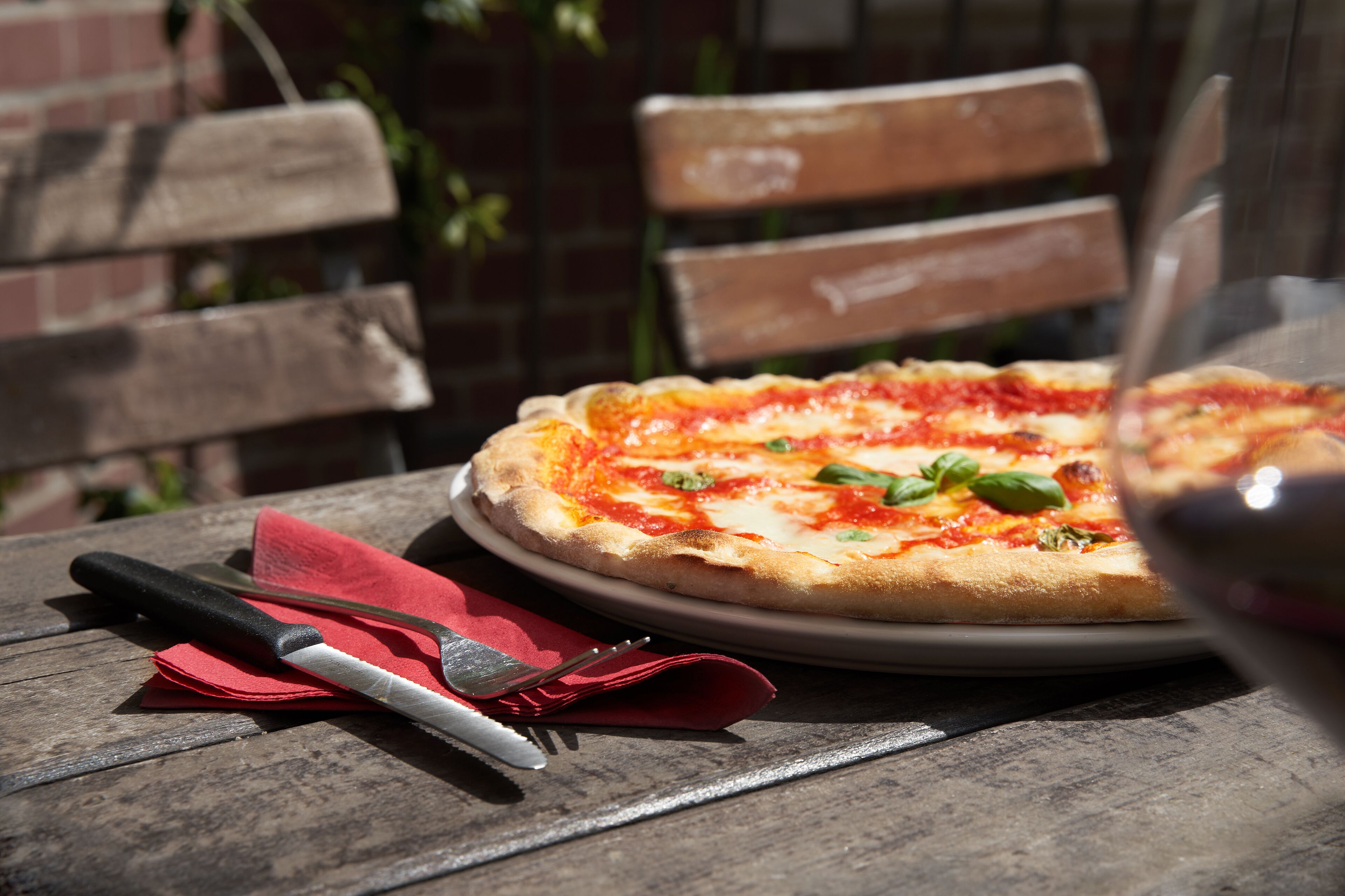 A pizza on a plate with a knife and fork on a wooden table.
