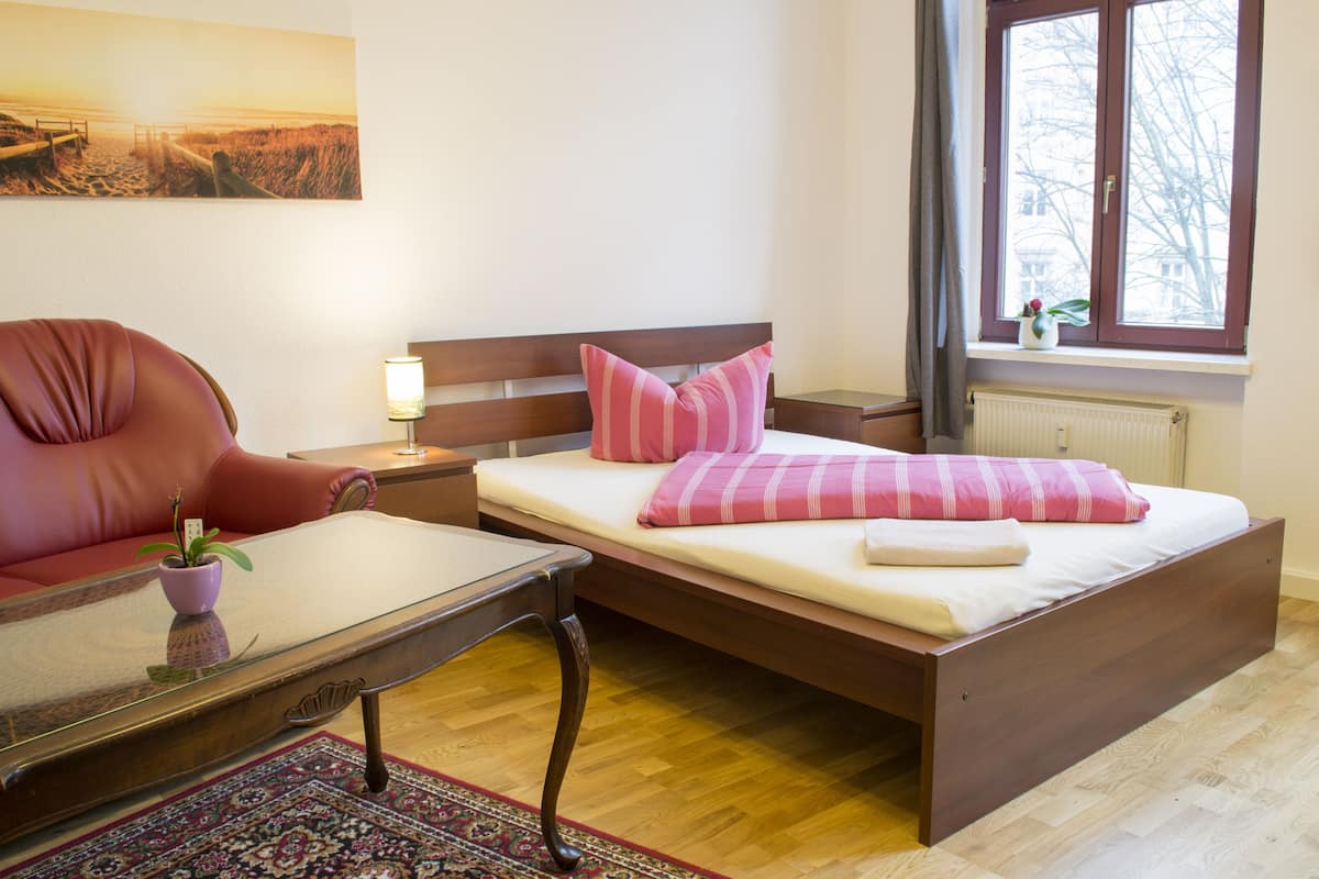 A bedroom with a wooden bed, a red chair, a small table, and a nightstand with a lamp.