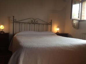 A neatly made bed with a headboard, two bedside lamps, and a window with blinds. - Lovely typical barn ,, in the heart of the most beautiful cities of Tuscany (MONTERIGGIONI (SIENA))